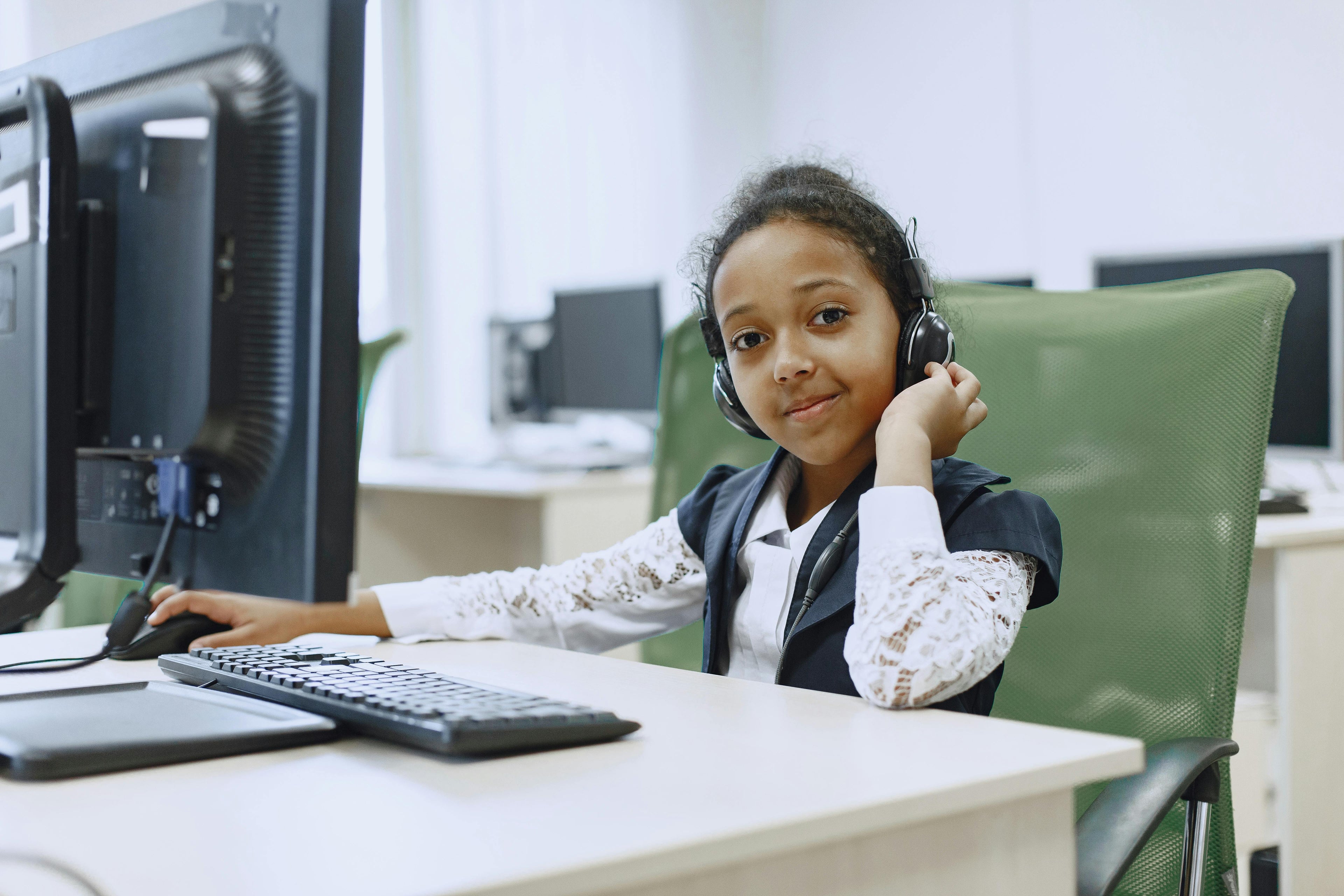 Child sitting at a computer desk with headphones on, smiling.
